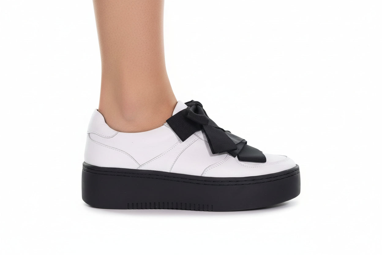 White sneaker with black platform sole and decorative strap on a white background